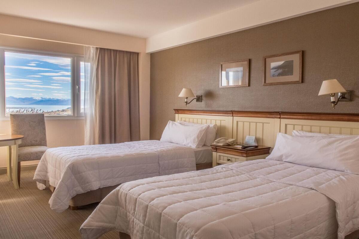 Camera d'albergo con due letti, una scrivania, una sedia, una finestra con vista e due lampade a parete.