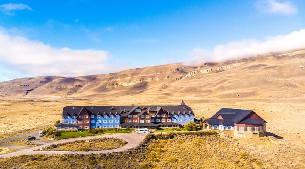 Un hotel con varias edificaciones, un estacionamiento y montañas al fondo.
