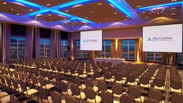A conference room with rows of chairs, a presentation screen, and a table with a banner for Alto Calafate Hotel & Spa.