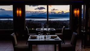 Un comedor con una mesa dispuesta para dos, ventanas amplias que ofrecen vistas a montañas y una masa de agua.