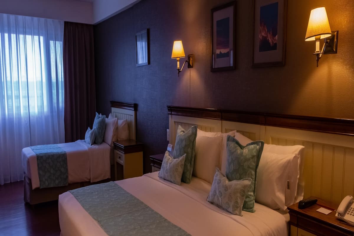 Una camera d'albergo con due letti, lampade ai comodini, un comodino con un telefono e quadri appesi alle pareti.