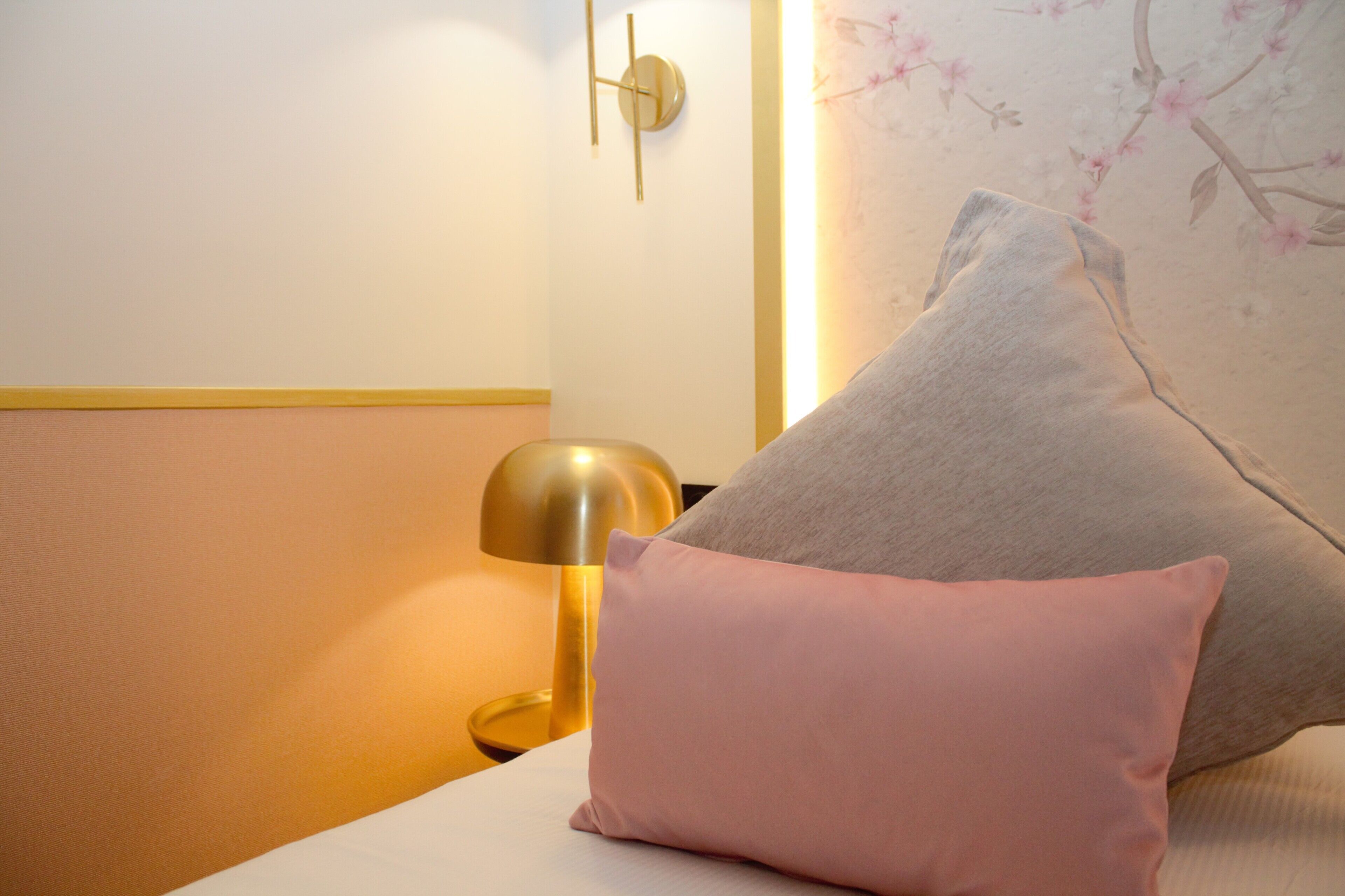 A room with a bed, a nightstand, a lamp, and a wall with a floral pattern.