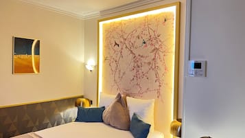 Ett hotellrum med en stor säng, en väggmonterad lampa, en tavla och en termostat.