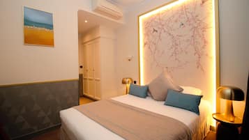 Quarto de hotel com cama, luminárias de cabeceira, ar-condicionado fixado na parede, um quadro e uma porta que dá para um armário.