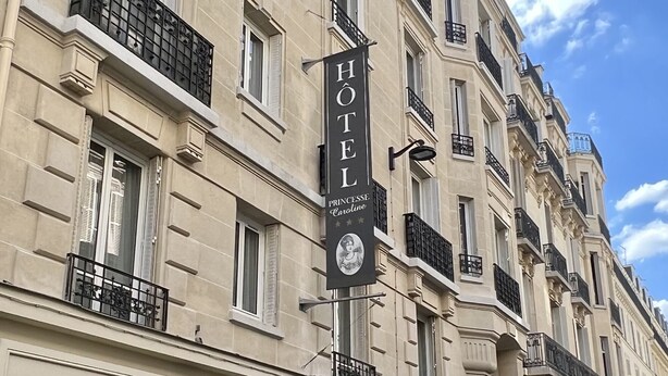 Un edificio histórico de varios pisos, con un letrero llamativo que dice 'Hôtel Princesse Caroline' y un escaparate azul.