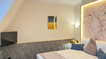 A hotel room with a bed, a flat-screen TV mounted on the wall, a painting above the bed, and a decorative wall panel.