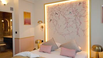 A hotel room with a bed, pillows, a nightstand, a lamp, a wall with a floral mural, and a bathroom visible in the background.
