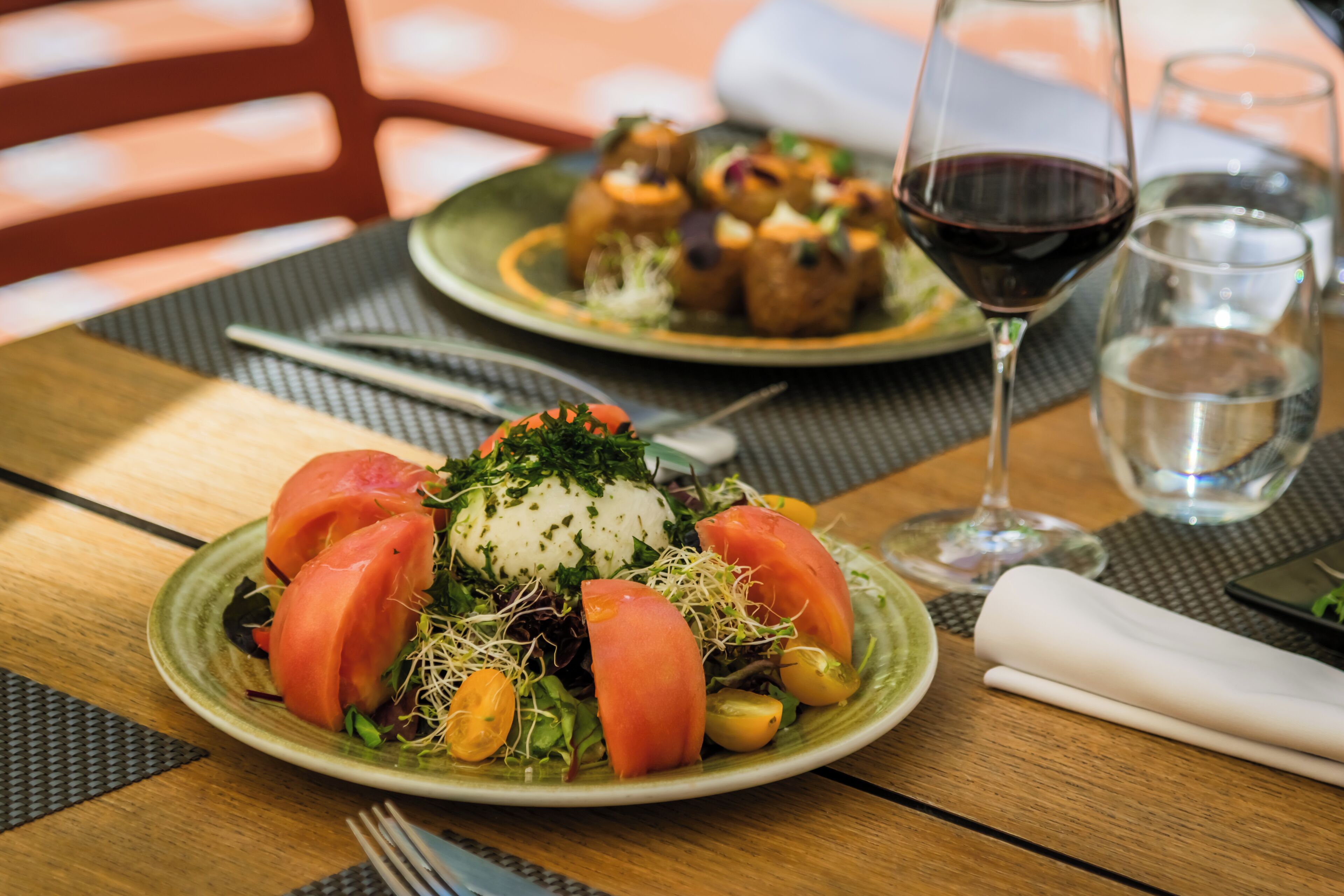 A dining table with plates of food, a glass of red wine, and a napkin.