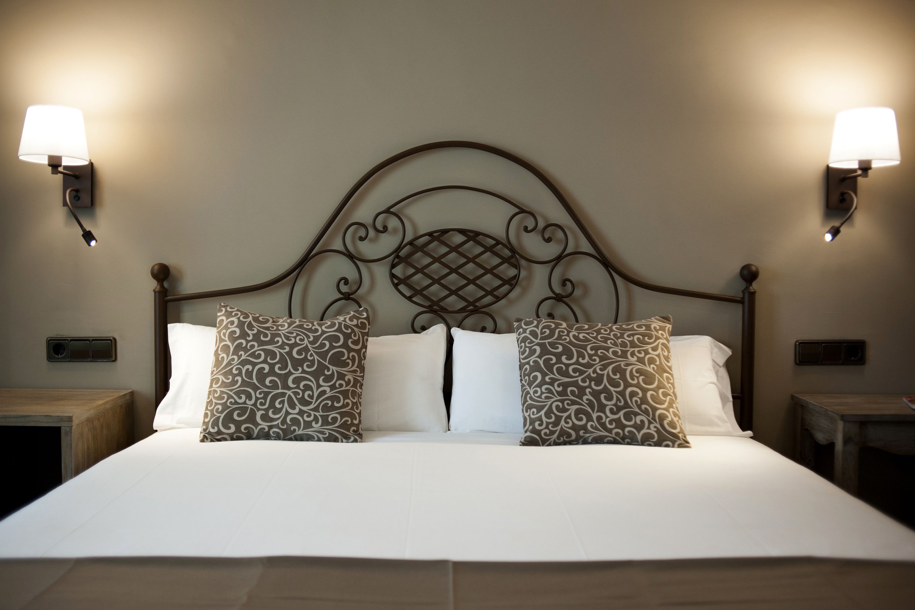 A neatly made bed with a headboard, two wall-mounted lamps, and a small bedside table.