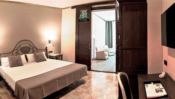 A hotel room with a bed, bedside tables, a desk with a chair, and a door leading to a balcony.