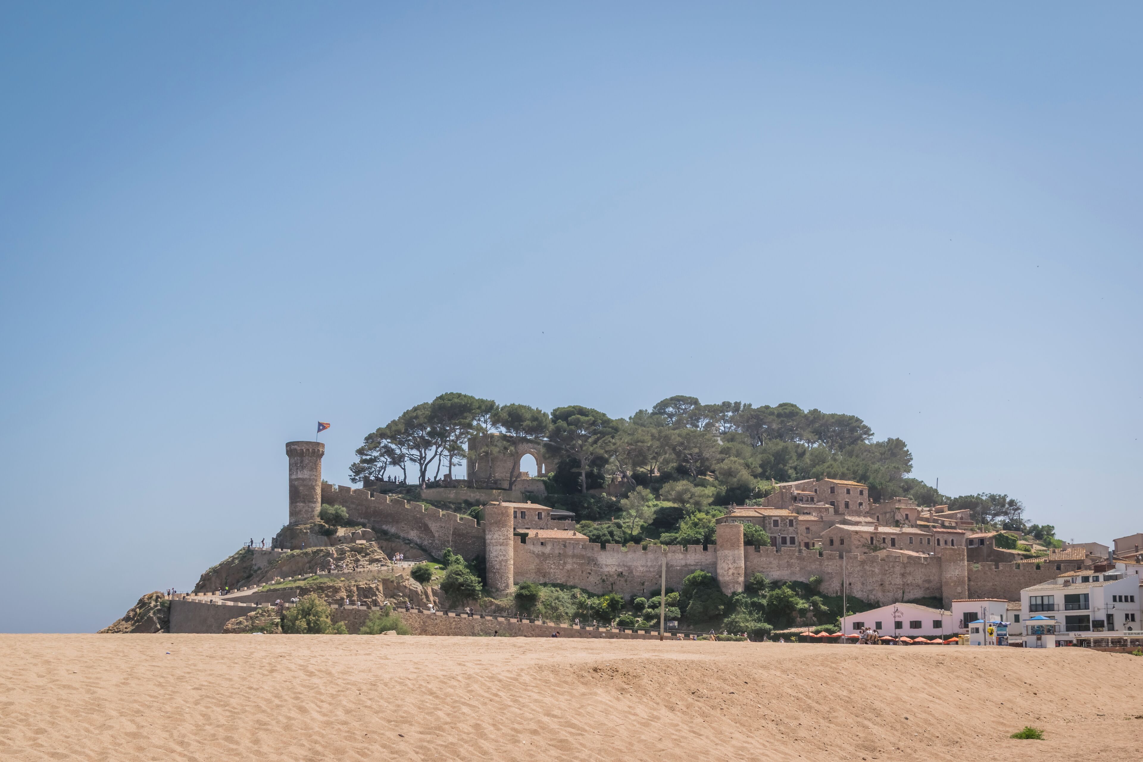 A coastal fortification with a tower, surrounded by buildings and vegetation.
