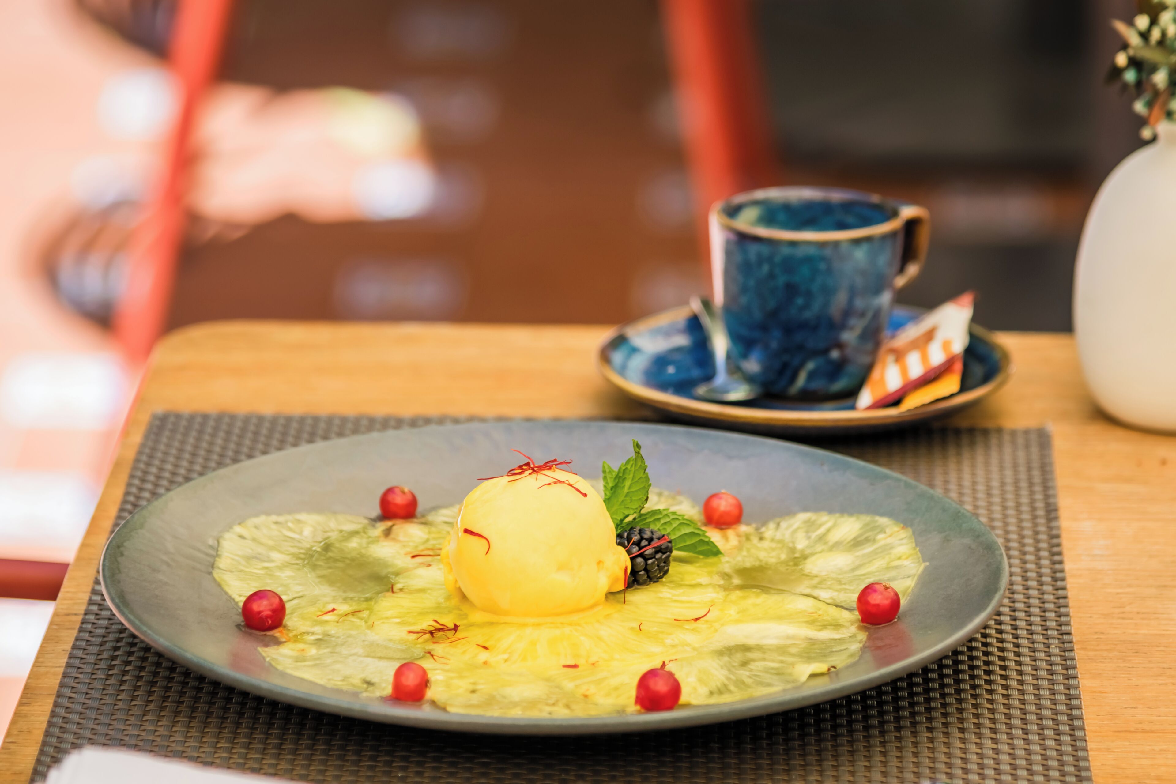 A dessert plate with a scoop of ice cream, garnished with berries and mint leaves, on a textured mat.
