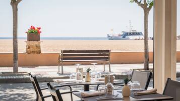 An outdoor dining area with tables set for two, a stone planter with flowers, and a bench.