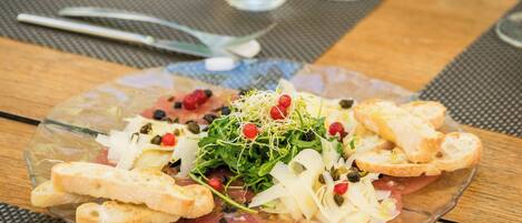 A clear glass plate with a salad, bread, and a water glass on a wooden table.