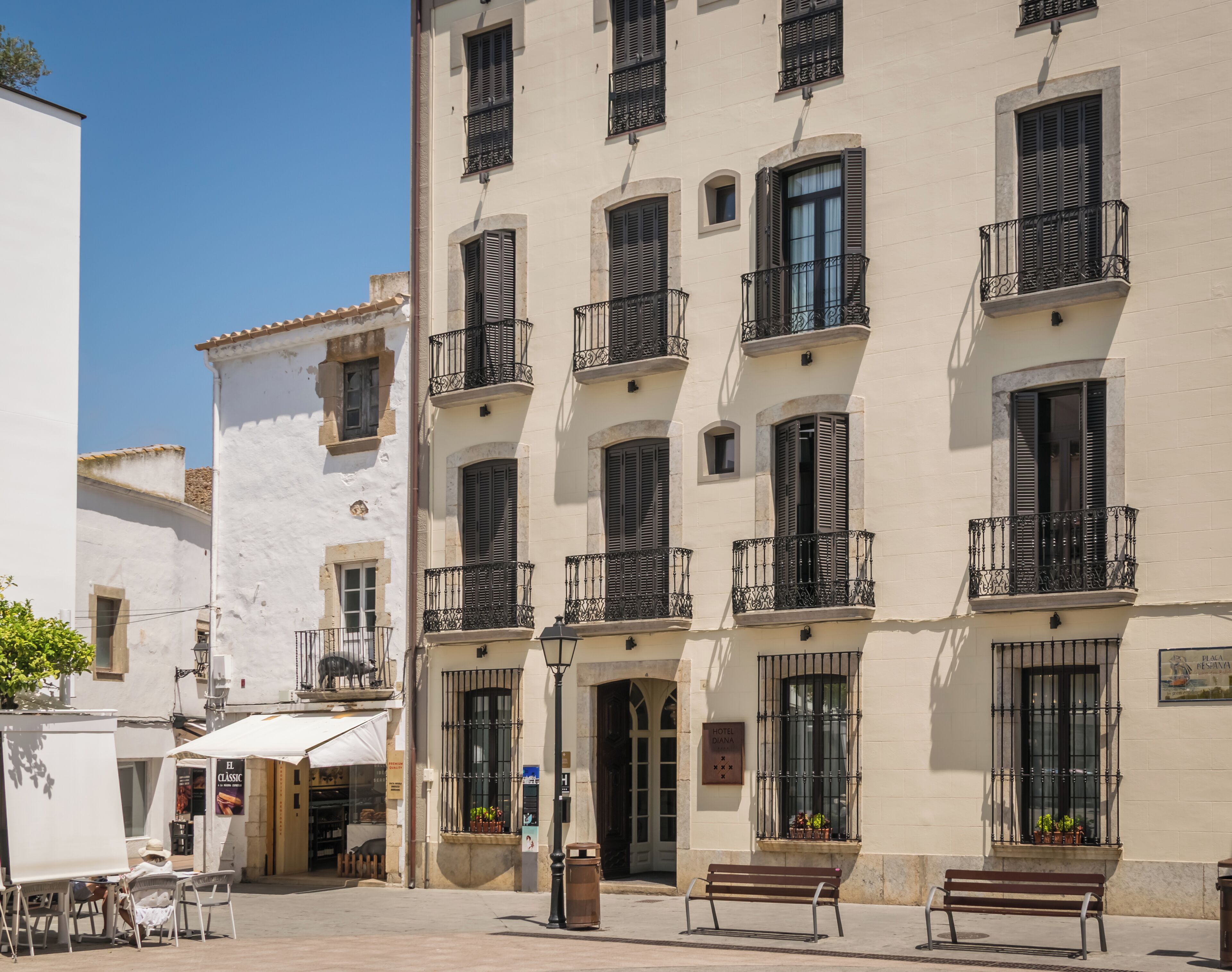 Un edificio de varios pisos con balcones, un café en la calle y bancos.