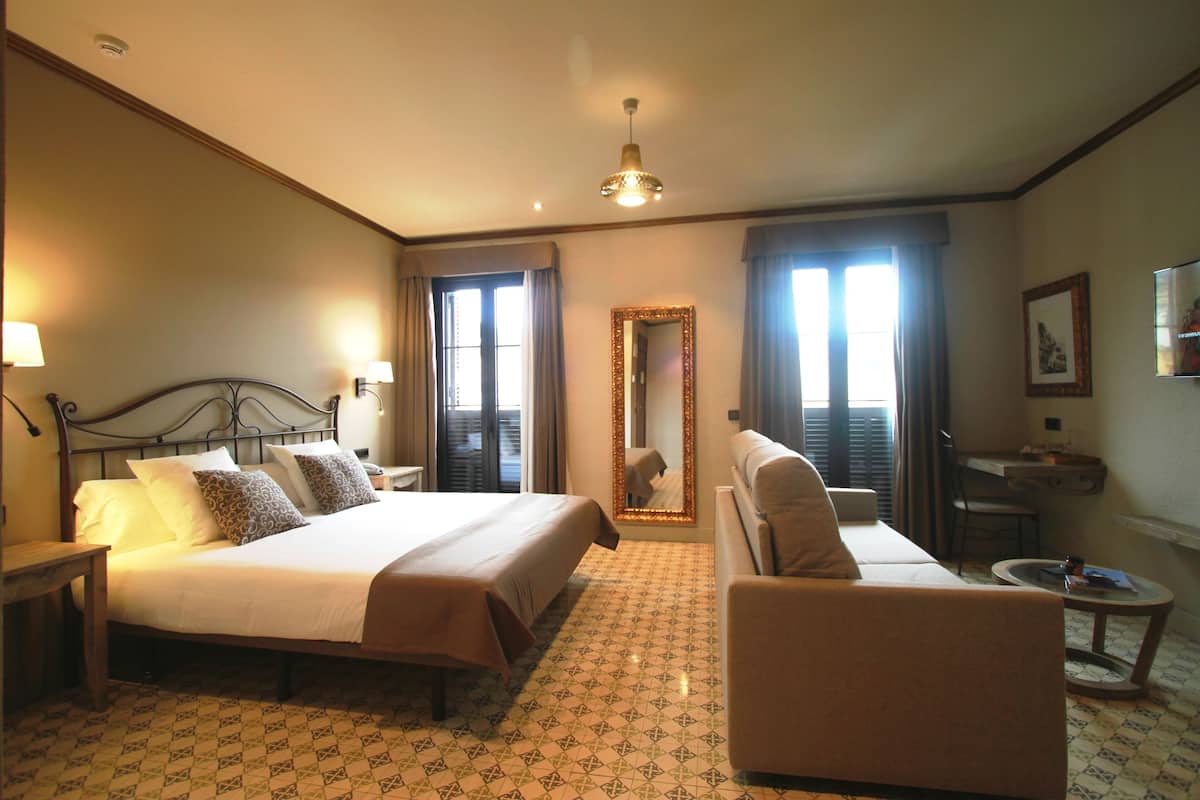 Una habitación de hotel con una cama grande, un sofá, una mesita y un espejo.
