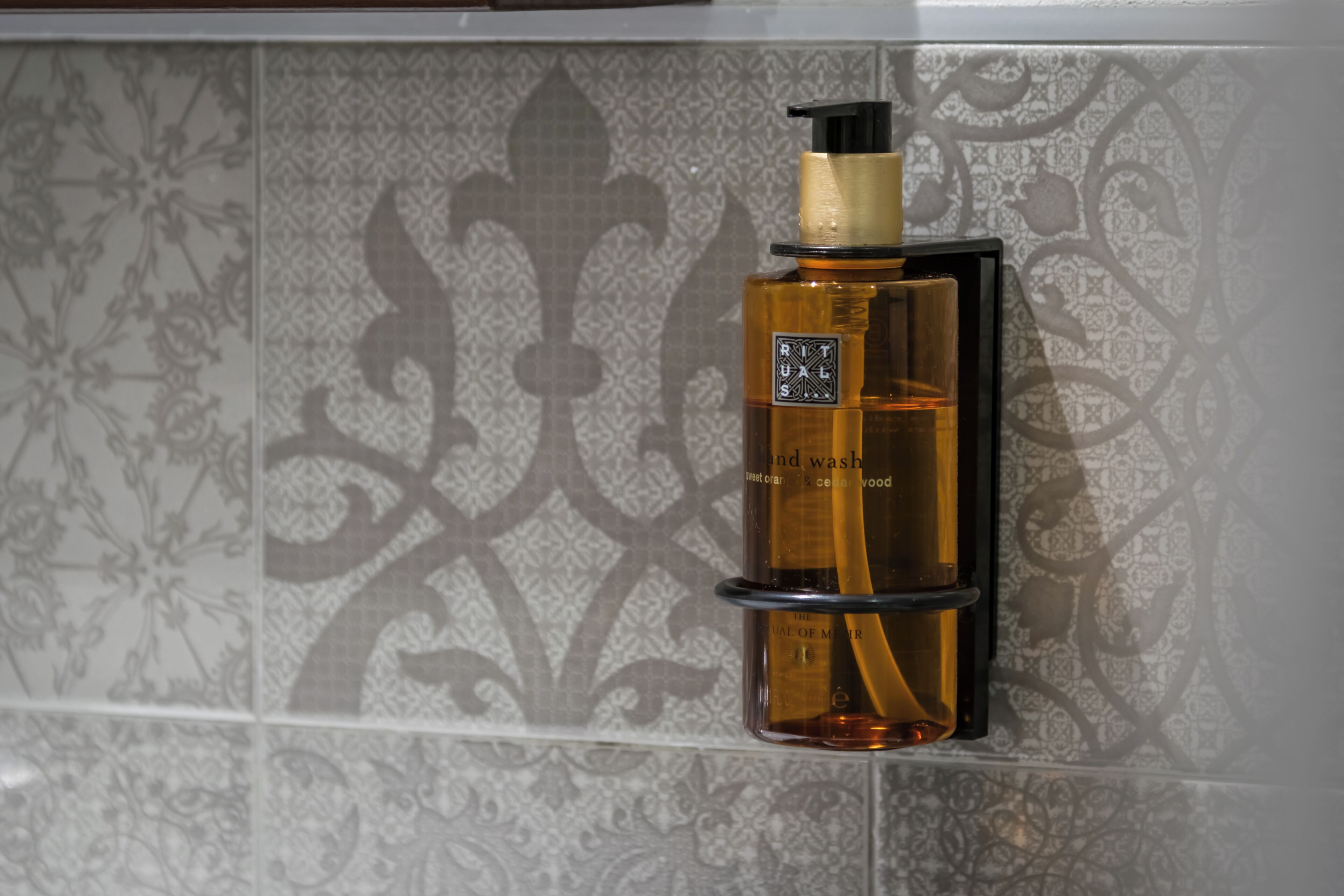A bottle of hand wash soap on a tiled wall.