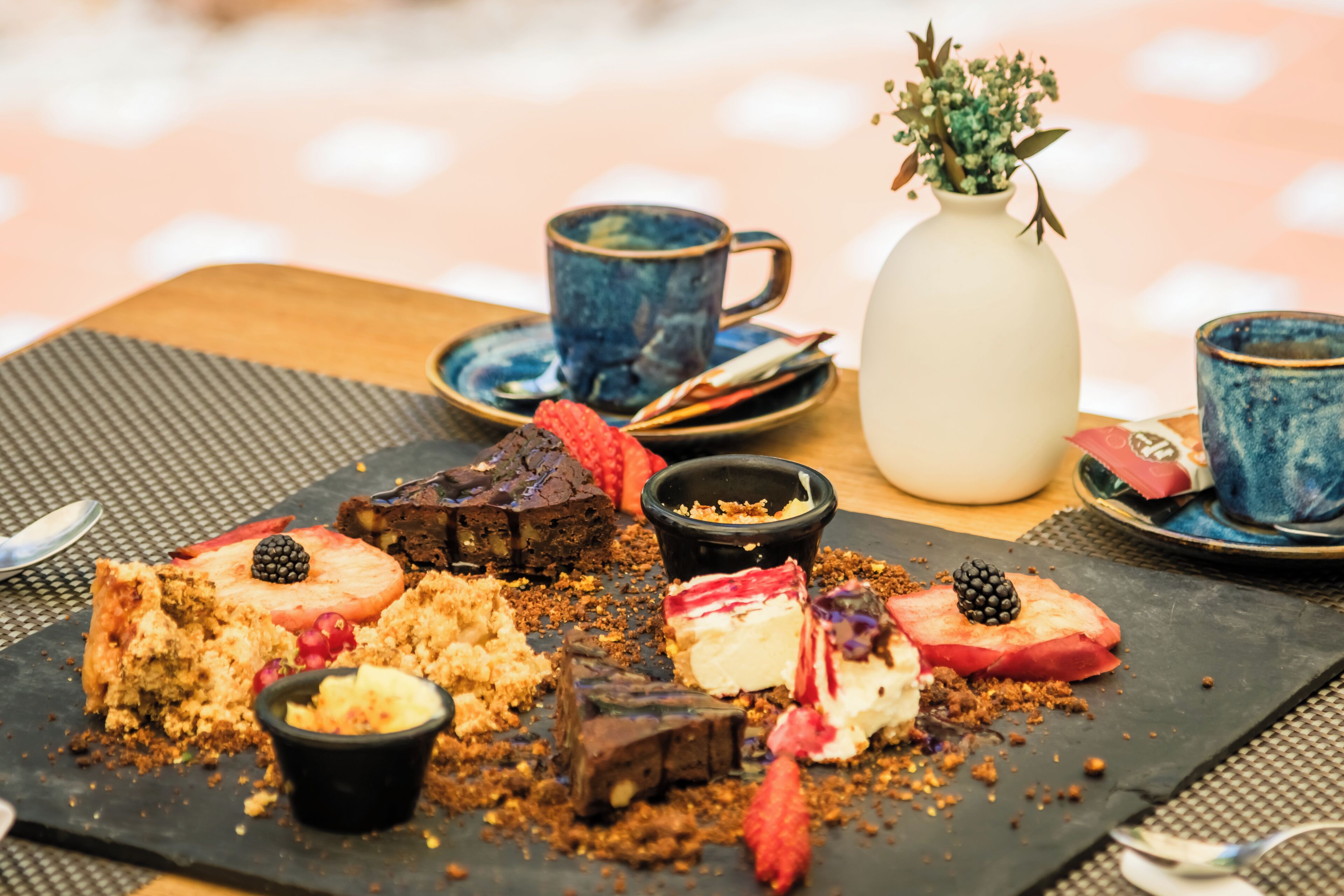 A dessert platter with various sweets and a vase of flowers on a table.