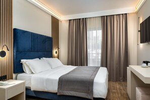 A modern hotel room with a large bed, a bedside table, a desk, and a TV. - Palatino Hotel (Zakynthos)