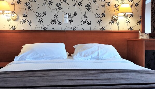 A hotel room with a bed, two wall-mounted lamps, and a floral wallpaper design. - Palatino Hotel (Zakynthos)
