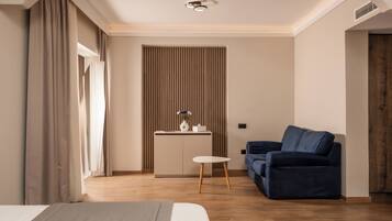 Una habitación de hotel moderna con una cama, un sofá azul, una mesita y una zona de kitchenette.