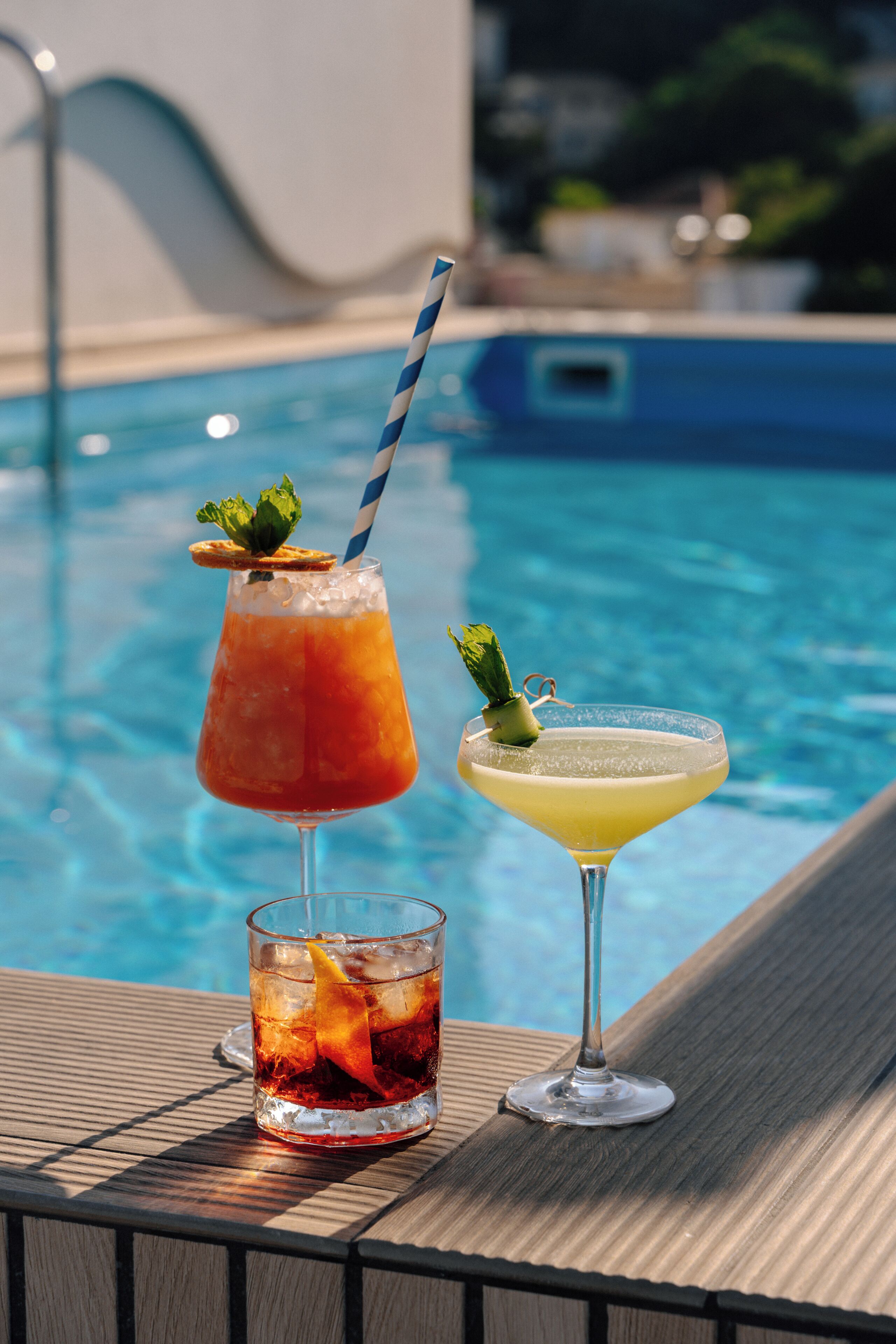 Two drinks on a poolside table with a pool in the background.
