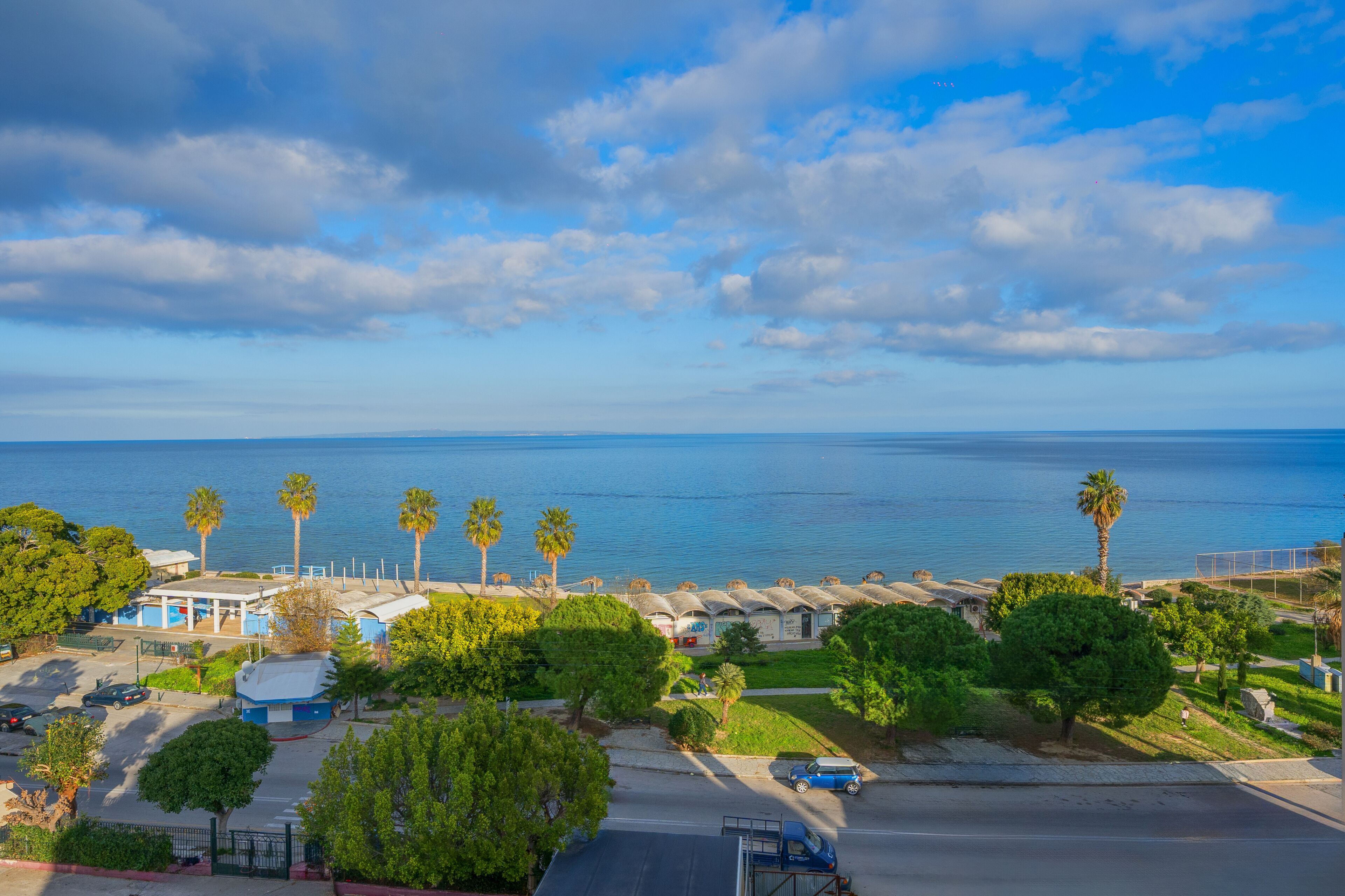 A coastal view with a parking lot, palm trees, and a clear sky.