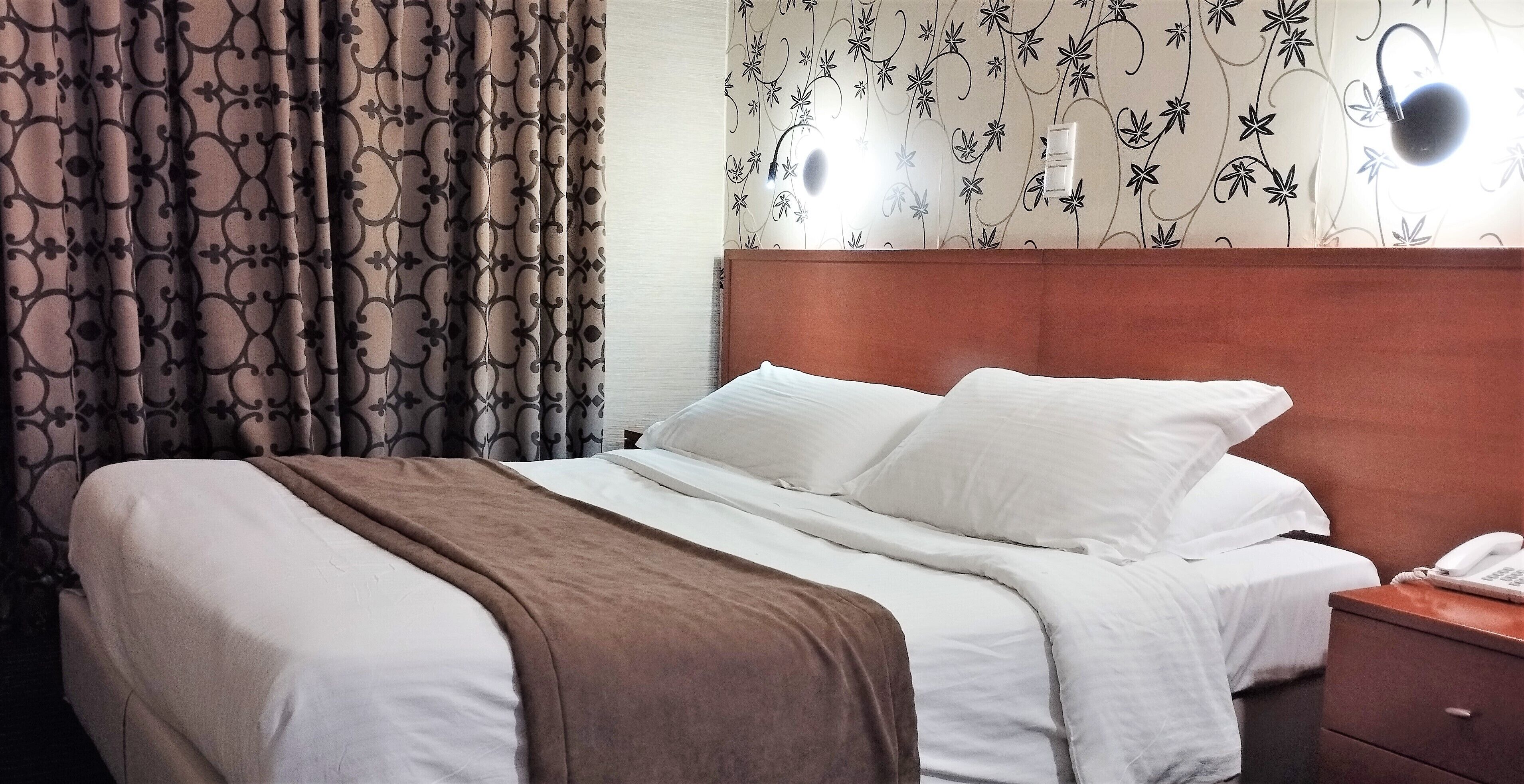 Ein Hotelzimmer mit einem Bett, einem Nachttisch und einer Wand mit floralem Wandpapier.