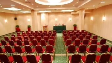 A conference room with rows of red chairs, a podium, and two potted plants.