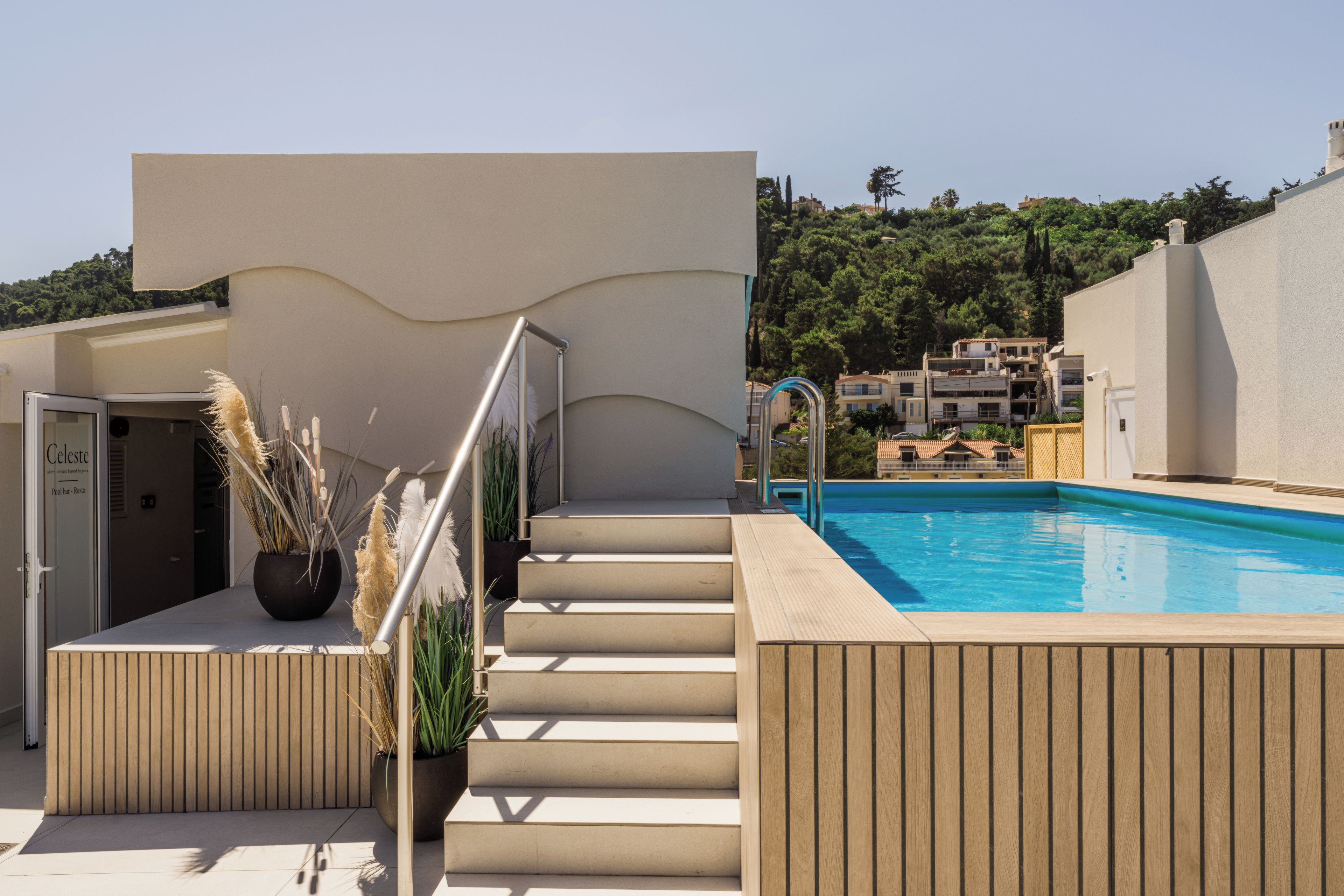 A pool area with steps leading to a building entrance, surrounded by greenery and a clear sky.