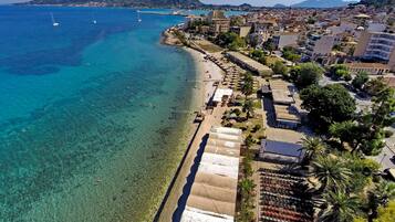 An aerial view of a coastal town with a beach, clear blue waters, and a mountain in the background.