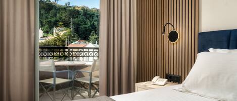 A hotel room with a bed, a desk, a chair, a phone, and a view of a balcony with a table and chairs.