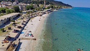 Una playa costera con aguas cristalinas, tumbonas, sombrillas y un paseo marítimo.