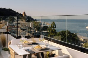 A dining table with a bowl of food, wine glasses, and a smartphone on a balcony overlooking a coastal cityscape. - Palatino Hotel (Zakynthos)