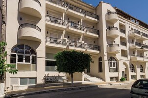 Un hotel de varios pisos con balcones, un árbol en primer plano y un coche estacionado en la calle.
