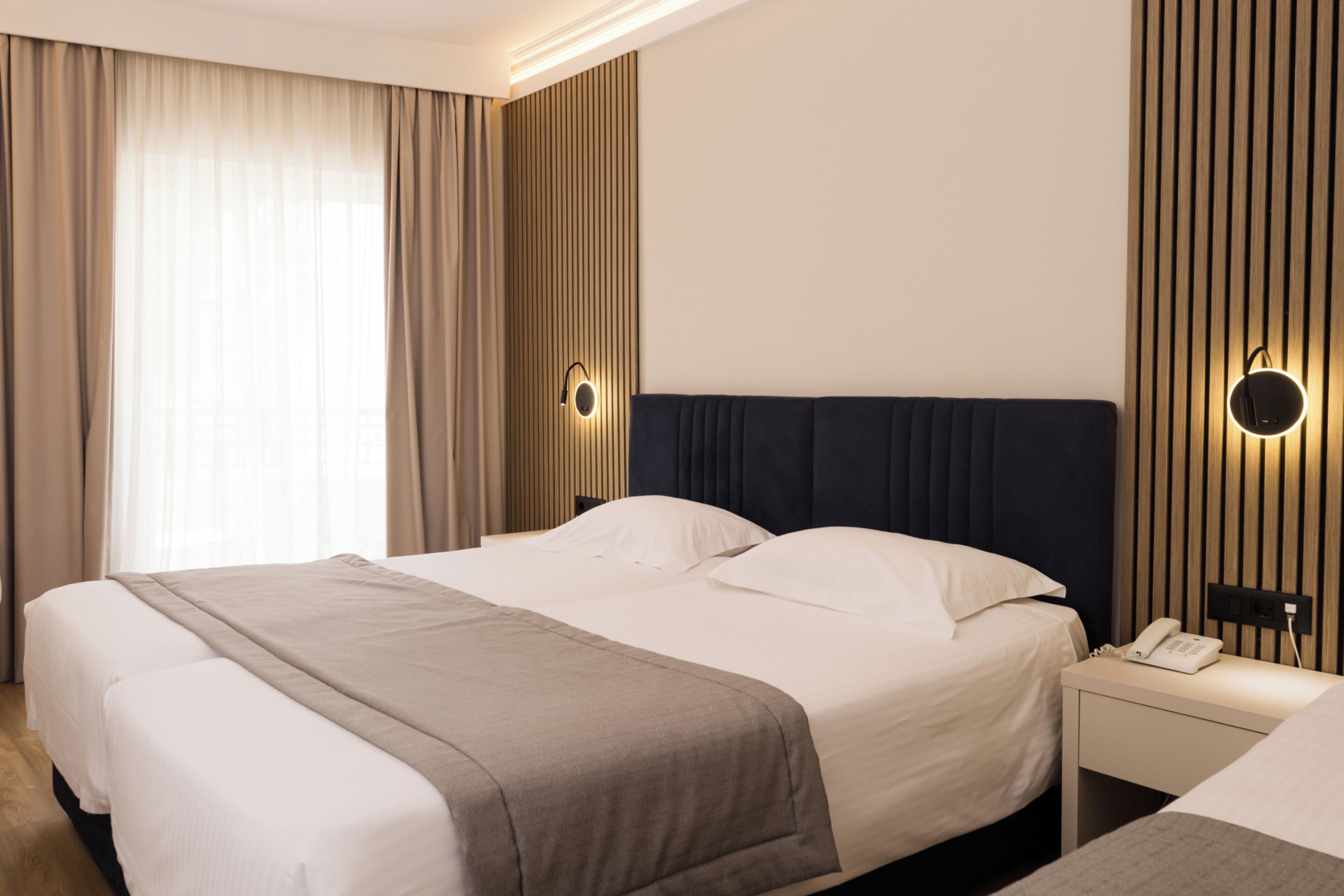 Une chambre d’hôtel avec un grand lit, une table de chevet avec un téléphone et un luminaire fixé au mur.