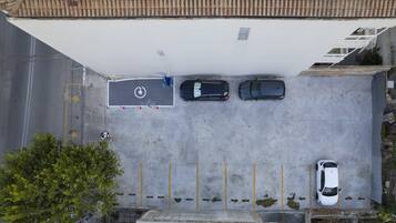 Vista aérea de um estacionamento com três carros estacionados em vagas designadas, uma área coberta e uma árvore em primeiro plano.