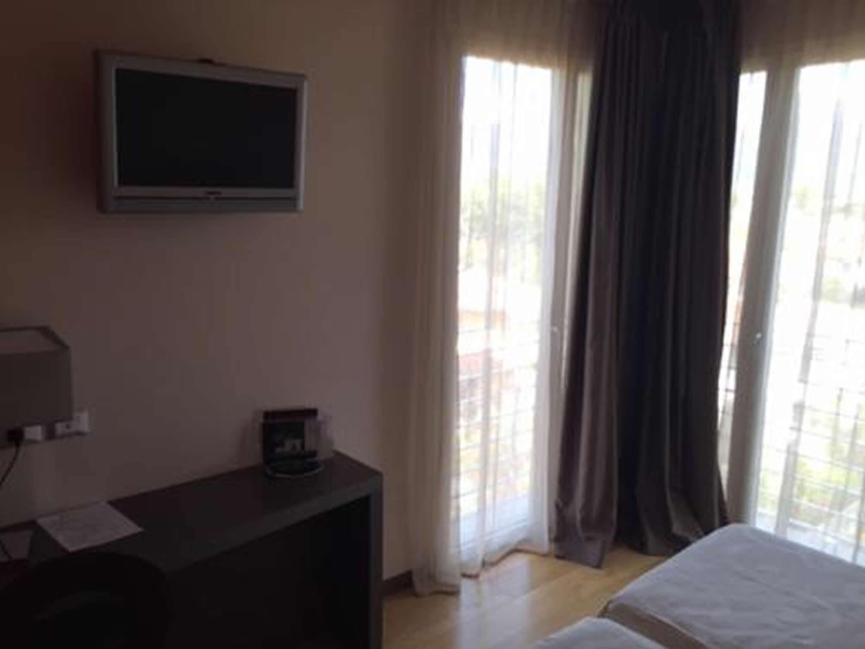 Une chambre d’hôtel avec un lit, un téléviseur fixé au mur, une petite table avec une machine à café et une fenêtre avec des rideaux.