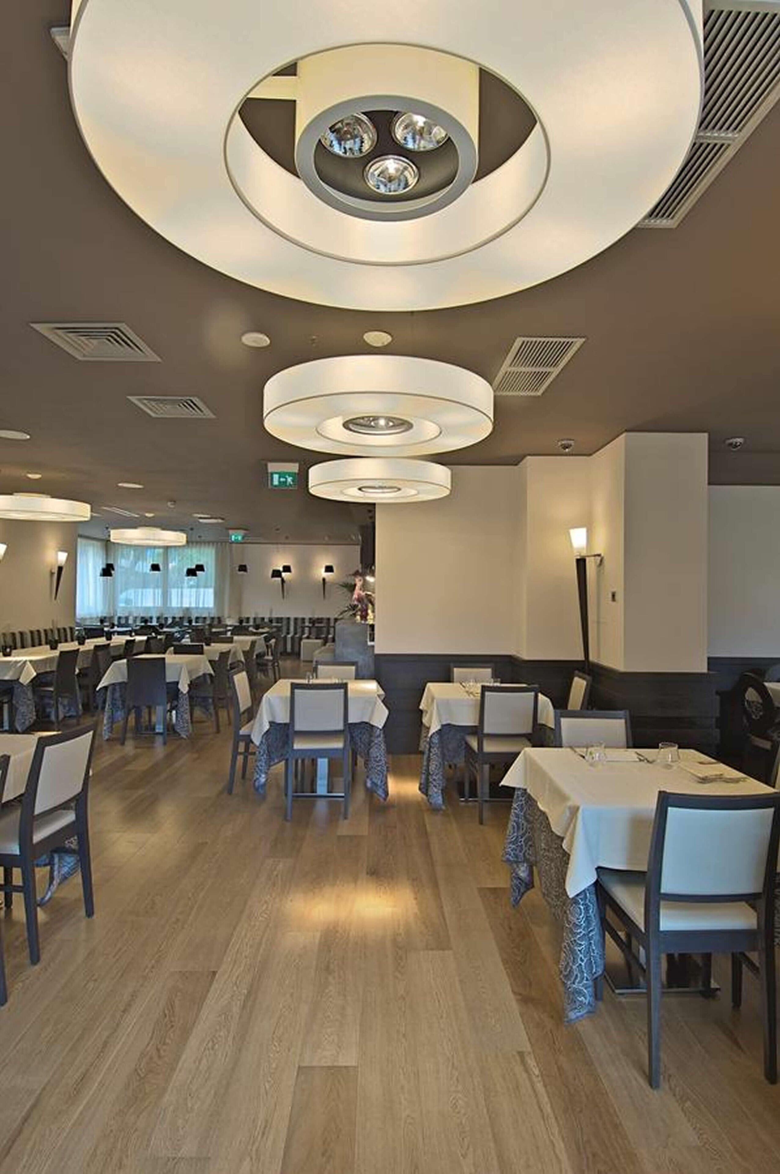 A spacious restaurant with multiple dining tables, circular ceiling lights, and a modern interior design.