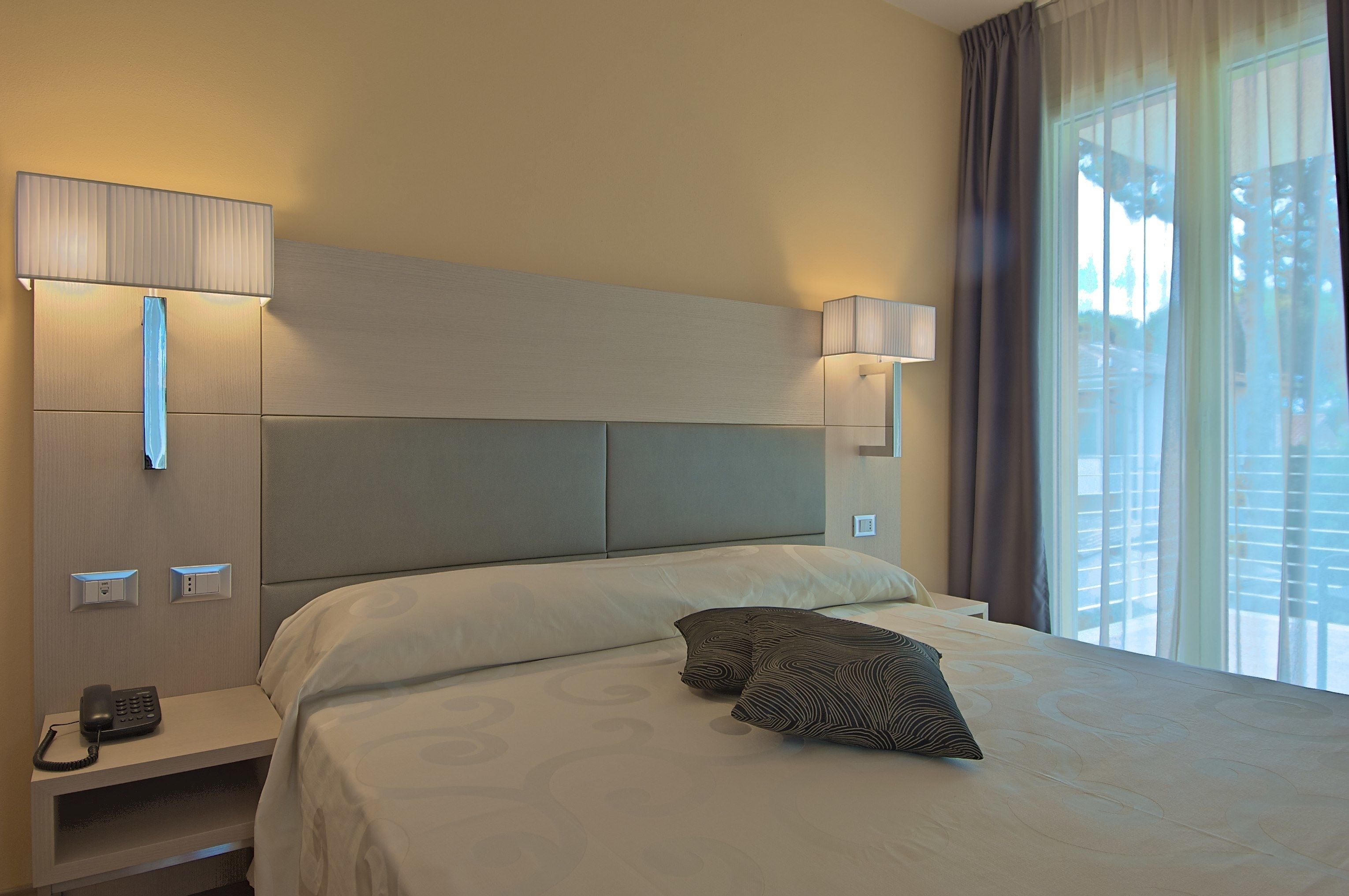 A hotel room with a large bed, bedside lamps, a telephone, and a window with curtains.