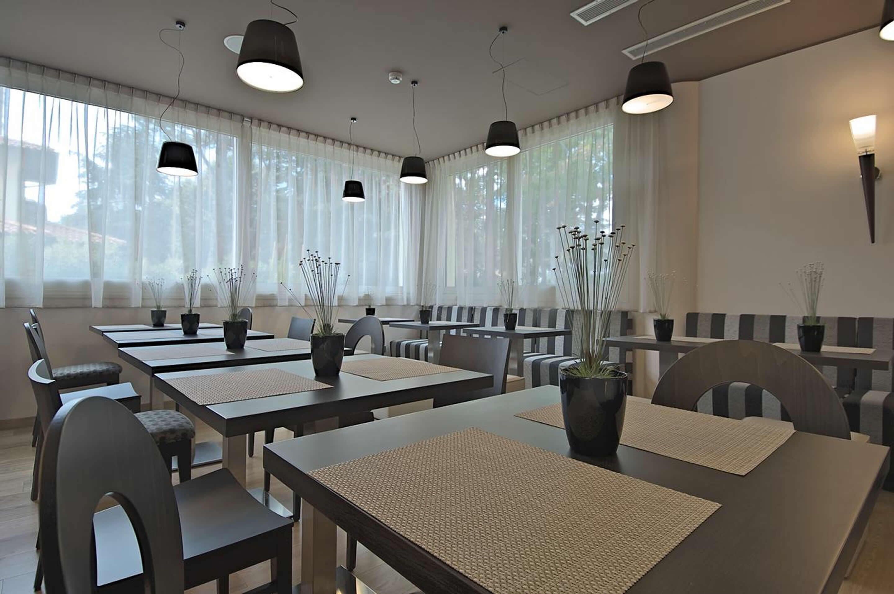 A modern dining area with tables and chairs, potted plants, and pendant lighting.