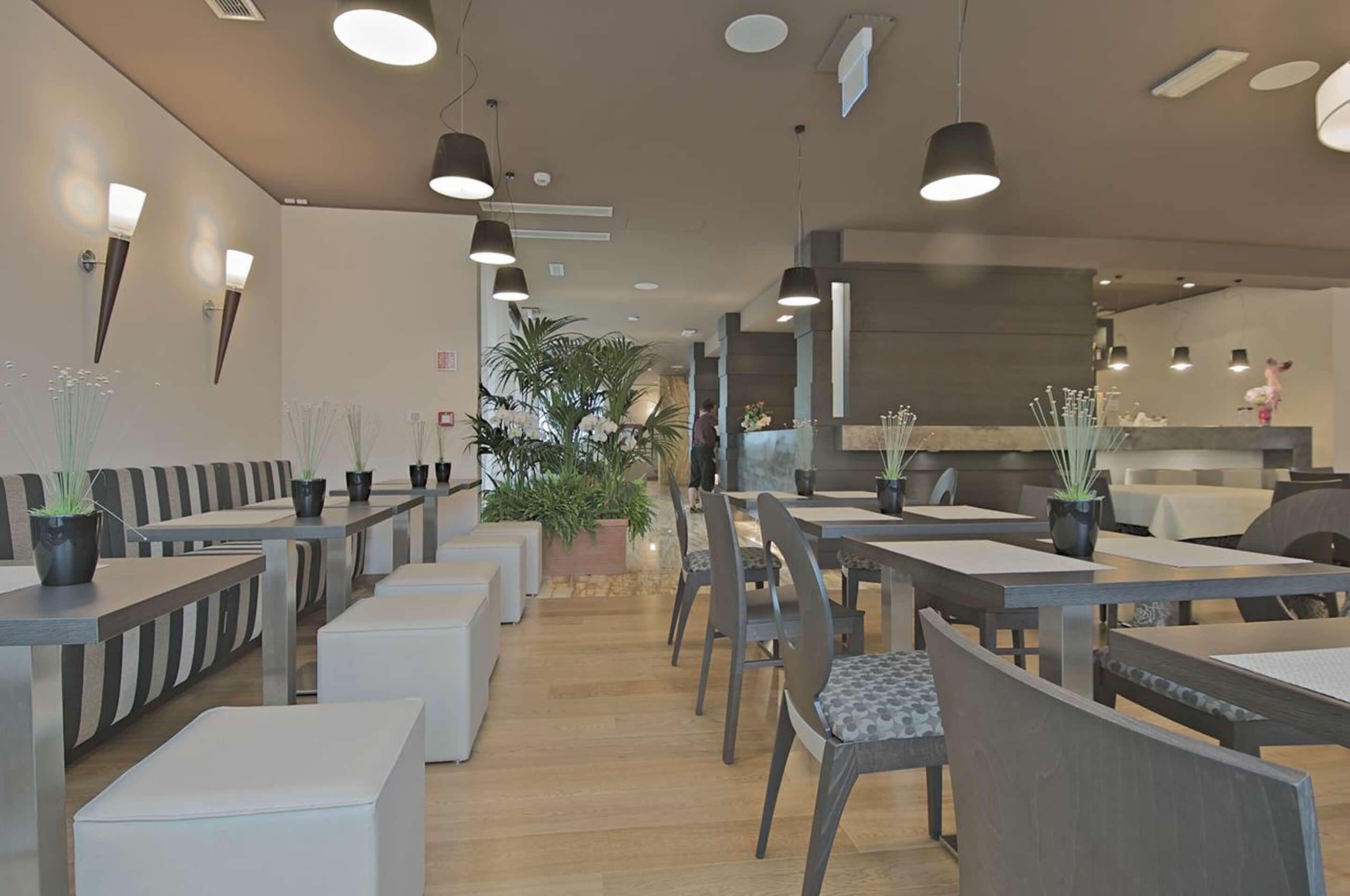 Een modern restaurantinterieur met hoge tafels en stoelen, hangende verlichting en potplanten.