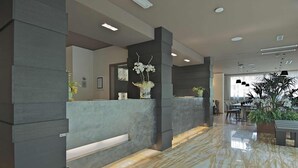 Un área de recepción moderna con suelo de mármol, mostrador gris y plantas en macetas.