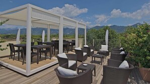 Un patio al aire libre con una pérgola blanca, muebles de mimbre oscuro y vistas a las montañas.