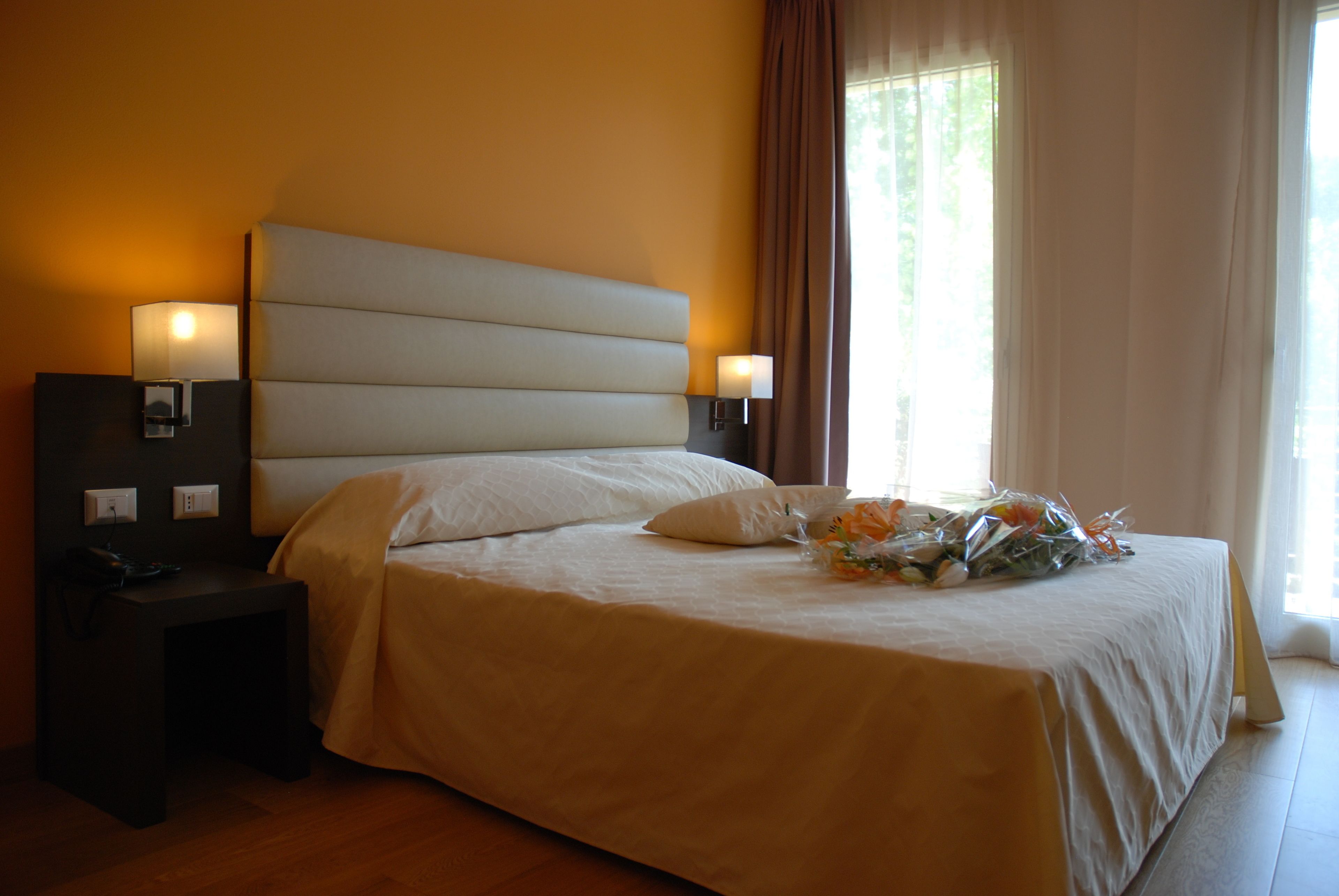 Una cama bien hecha con cabecera, lámparas de noche y un ramo de flores sobre la cama.