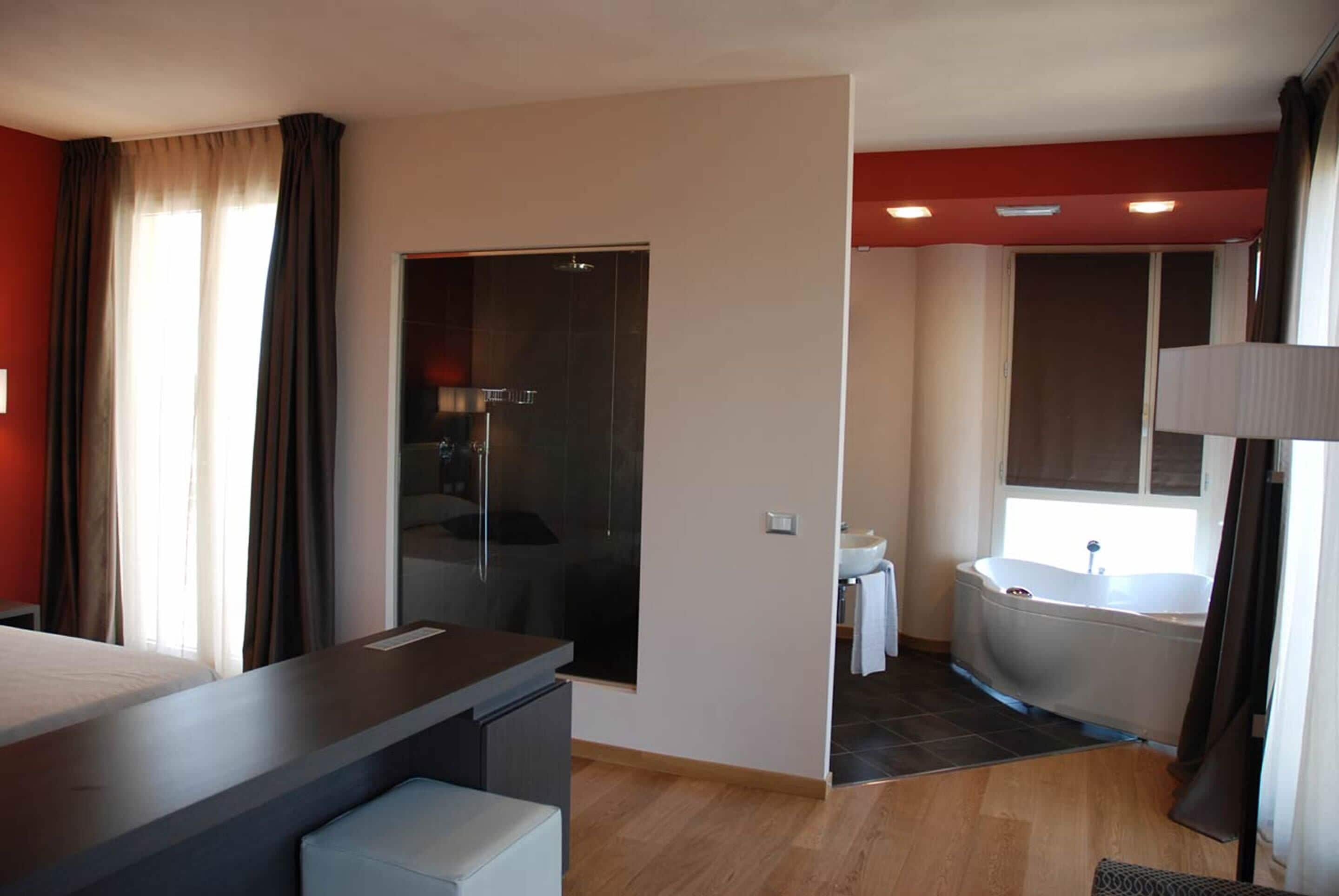 A modern hotel room with a large bed, a separate bathroom with a bathtub, and a shower area.