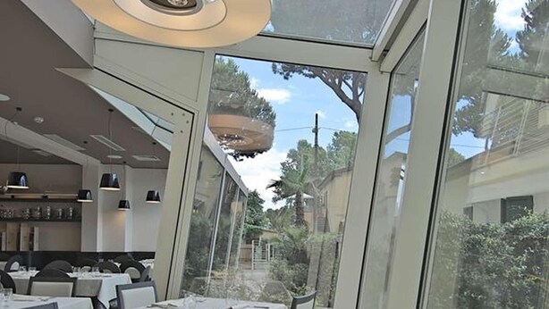 Un comedor moderno con mesas dispuestas para dos, amplias ventanas que ofrecen vistas al exterior y una lámpara colgante de diseño contemporáneo.