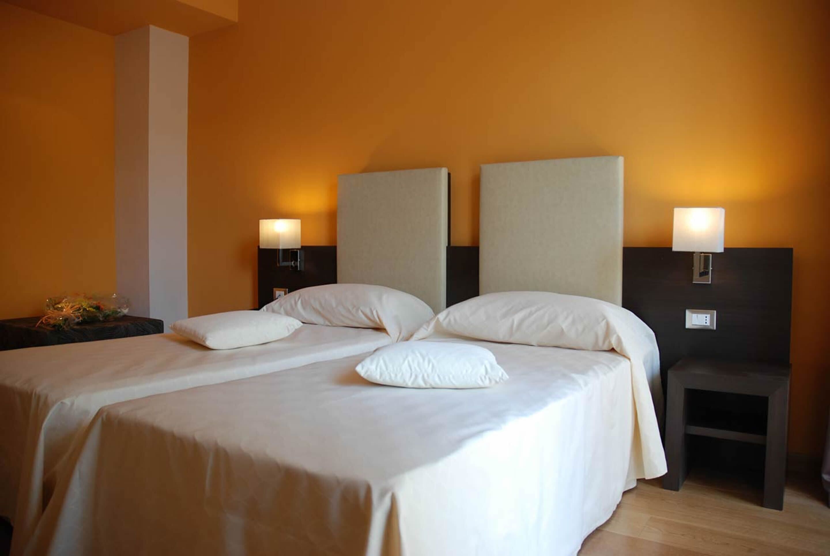 Una cama doble con dos almohadas, una mesita de noche con lámpara y un pequeño taburete.
