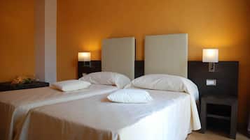 A double bed with two pillows, a nightstand with a lamp, and a small stool.