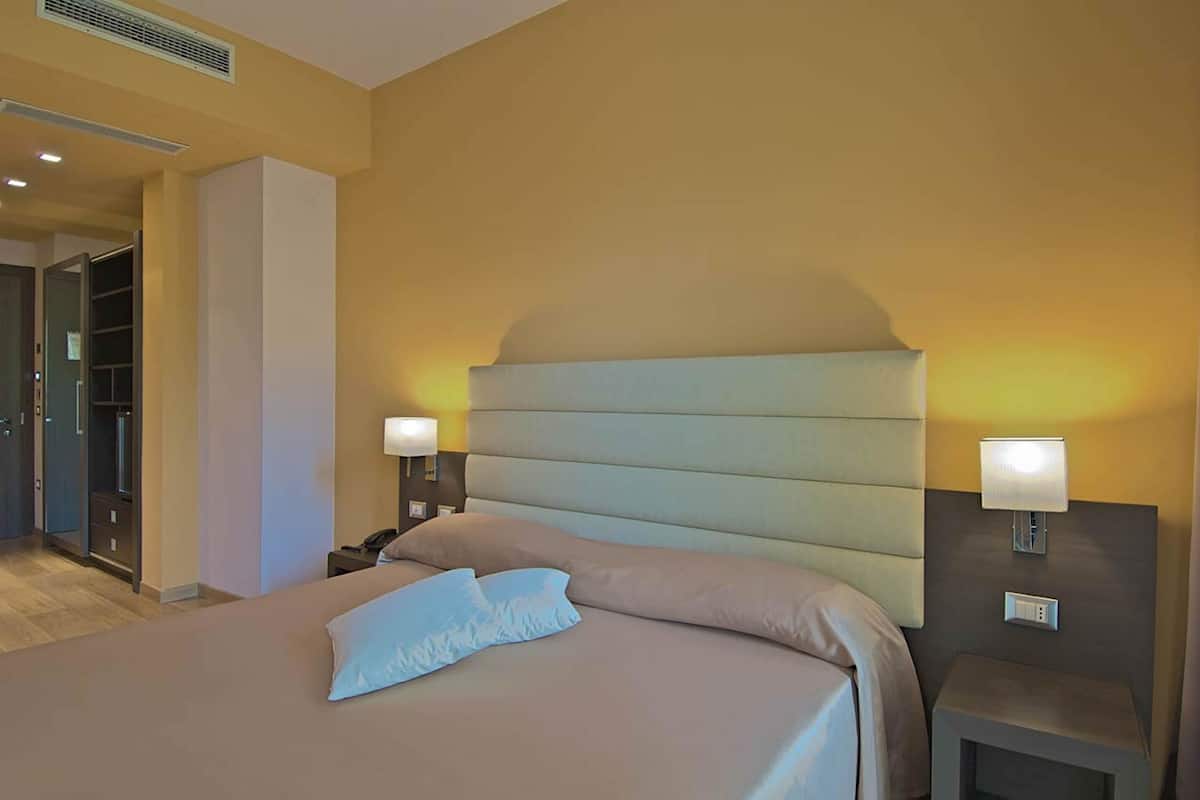 Una habitación de hotel con una cama grande, lámparas de noche, una mesita de noche y un armario.